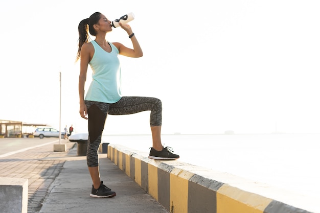 Foto de hermosa mujer corredor de pie al aire libre sosteniendo una botella de agua. Mujer fitness tomando un descanso después de ejecutar el entrenamiento.