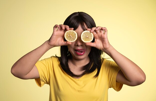 Foto foto de una hermosa mujer cubriendo los ojos con limones cítricos posando aislada sobre un fondo de pared amarillo
