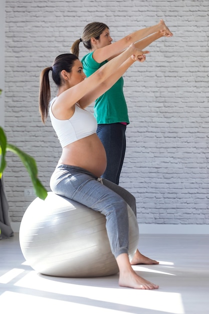 Foto foto de hermosa mujer embarazada con su fisioterapeuta haciendo ejercicios de pilates con pelota preparándose para el parto.