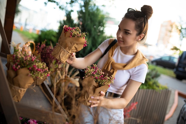 Foto de hermosa mujer morena atractiva europea vistiendo elegante camiseta blanca y jeans elige flores como regalo en una tienda de jardín de la calle en la ciudad