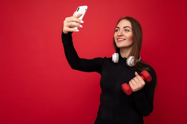 Foto de hermosa mujer morena joven positiva vistiendo ropa deportiva negra auriculares blancos