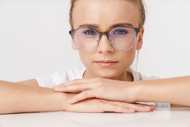 Foto de hermosa mujer seria en anteojos mirando a la cámara mientras se inclina sobre la mesa