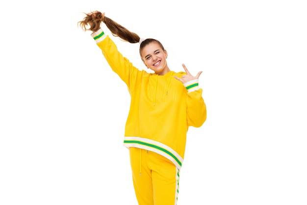 Foto de una hermosa niña sonriente con cabello oscuro con una cola de caballo en un elegante chándal amarillo con