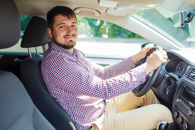 Una foto de un hermoso joven empresario feliz sonriendo a la cámara, sentado al volante de un coche.