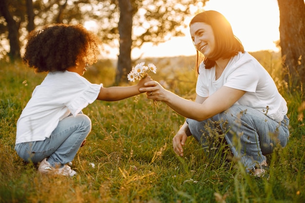 Foto de hija afroamericana regalar una flor a su madre caucásica. La chica tiene el pelo negro y rizado