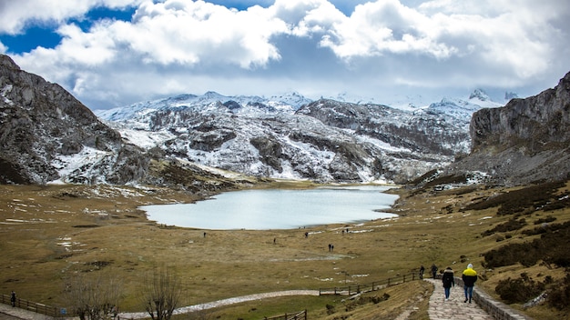 Foto hipnotizante de um cenário natural com um lago, montanhas nevadas e grandes nuvens fofas