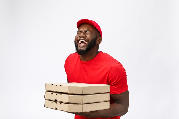 Foto de hombre afroamericano feliz del servicio de entrega en camiseta roja y gorra dando orden de comida y sosteniendo cajas de pizza