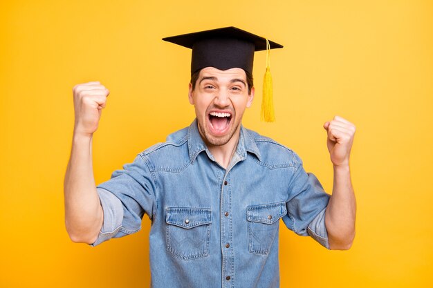 Foto de un hombre alegre con estilo de moda que se regocija en graduarse de la universidad gritando haciendo puños gritando pared amarilla de color vivo aislado