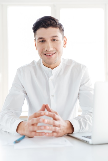 Foto de hombre alegre vestido con camisa blanca. Trabajo colaborativo. Mirando a la cámara.