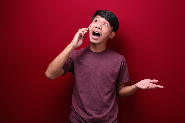 Foto de un hombre asiático sonriendo mientras recibe un teléfono aislado en un fondo rojo