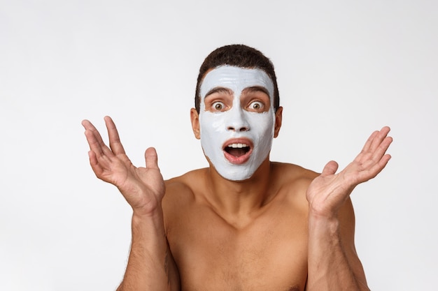 Foto de hombre sin camisa sonriendo y aplicando crema para la cara aislado en blanco