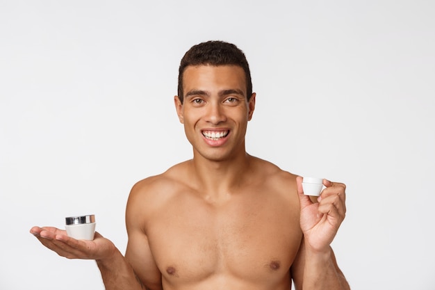 Foto de hombre sin camisa sonriendo y sosteniendo crema aislado sobre blanco