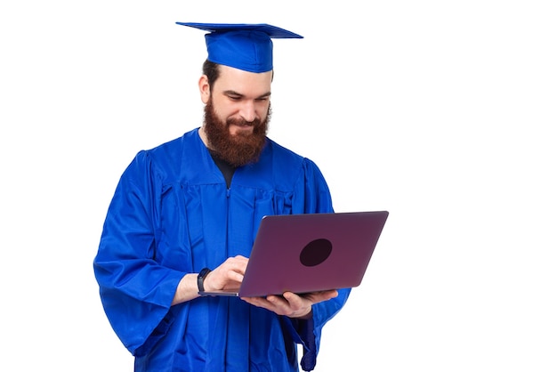 Foto de hombre estudiante en licenciatura azul con portátil sobre fondo blanco.