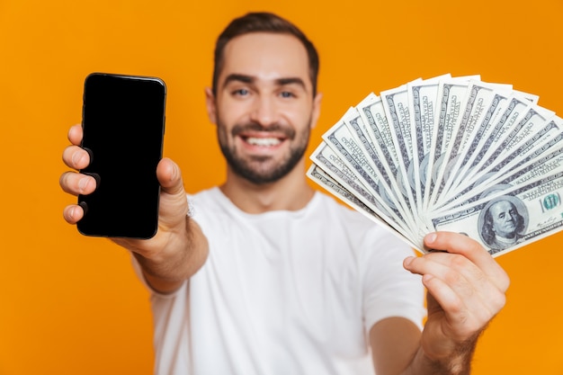 Foto de hombre europeo de 30 años en ropa casual con teléfono celular y ventilador de dinero, aislado