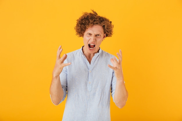 Foto de hombre furioso enojado con el pelo rizado levantando las manos con irritación, aislado sobre fondo amarillo