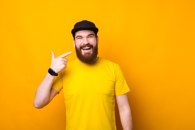 Foto de hombre guapo hipster barbudo apuntando a su sonrisa sobre pared amarilla