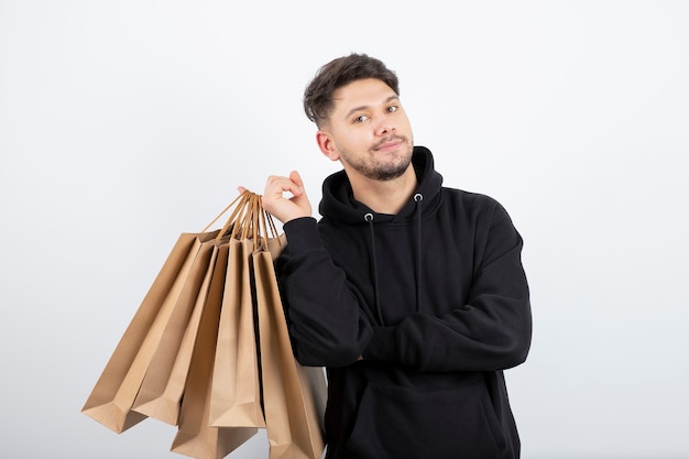 Foto de hombre guapo en sudadera con capucha negra que lleva un montón de bolsas de artesanía