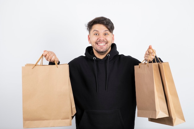 Foto de hombre guapo en sudadera con capucha negra que lleva un montón de bolsas de artesanía