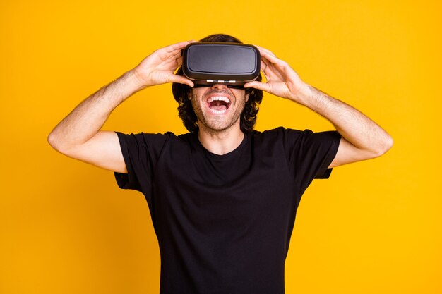 Foto de hombre joven disfrutar de la experiencia de realidad virtual con la boca abierta usar camiseta de casco vr fondo de color amarillo aislado