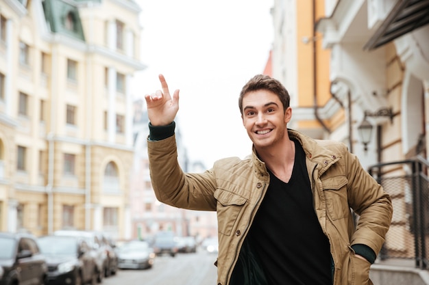 Foto de hombre joven feliz caminando por la calle y mirando a un lado mientras coge el coche.