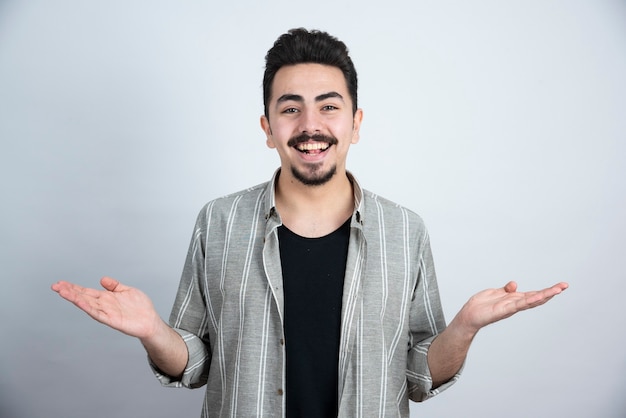 Foto de hombre joven en ropa casual de pie sobre una pared blanca.