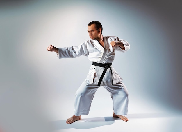 foto hombre en kimono blanco entrenando karate con fondo claro