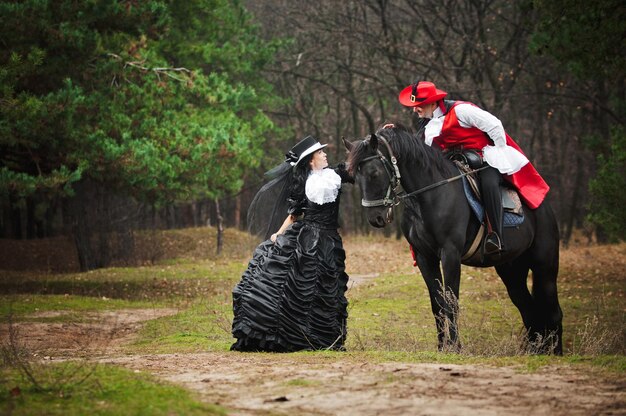 Foto de hombre y mujer en hermosos trajes de teatro cabalgando en el bosque