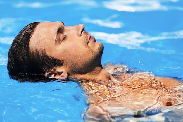 Foto foto de hombre musculoso relajarse en el agua azul de la piscina.