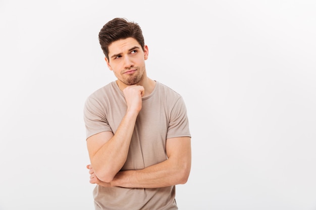 Foto foto de hombre pensativo apuntalando la barbilla y posando a un lado con mirada seria, aislado sobre la pared blanca