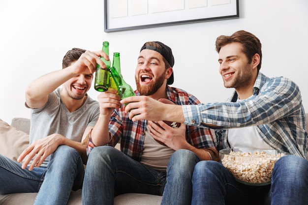 Foto de hombres felices gritando y celebrando la victoria de su equipo favorito, mientras ve el partido de fútbol con cerveza y palomitas de maíz