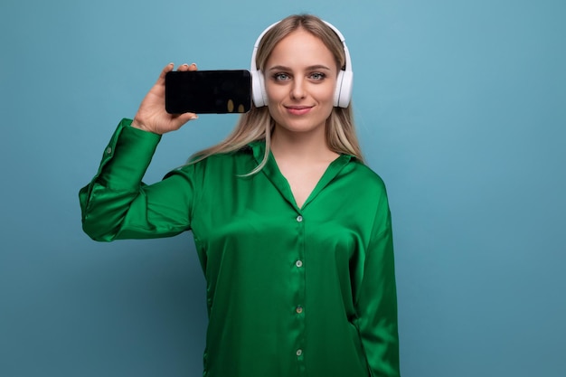 Foto horizontal de elegante mulher europeia segurando smartphone com tela voltada para frente em azul