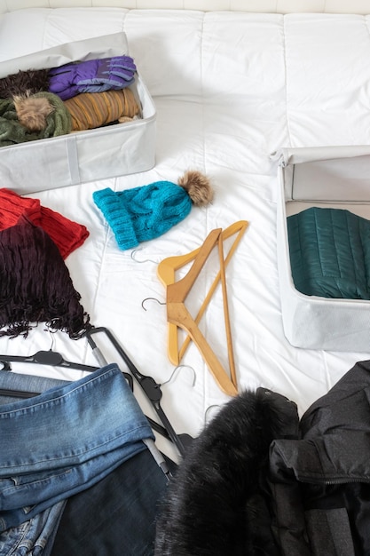 Foto foto horizontal de um quarto com roupas de inverno deitadas em cima da cama para serem coletadas dentro das caixas de tecido fazendo uma mudança de armário