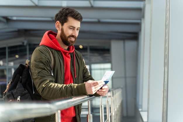 Foto horizontal do terminal do aeroporto interior homem confiante e bem-vestido. Ele segurando o passaporte nas mãos e olhando para o bilhete com um sorriso de prazer