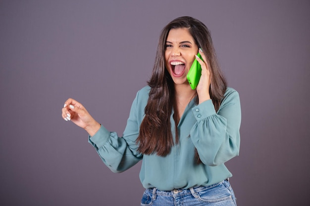 Foto horizontal Hermosa mujer brasileña con ropa casual Jeans y camisa verde en llamada de voz con smartphone