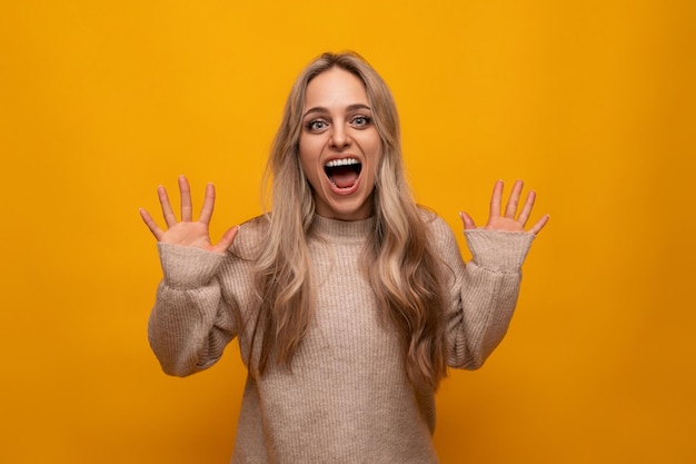 Foto horizontal de una joven rubia gritando sobre un fondo amarillo