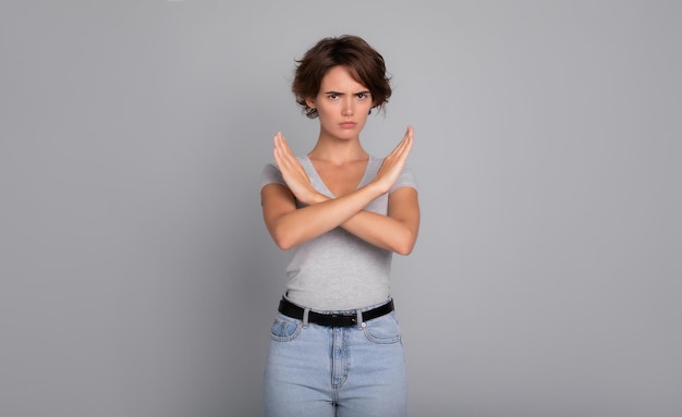 Foto foto horizontal de una joven seria con el pelo corto y rizado muestra las manos cruzadas sin parar símbolo prohibido o signo aislado sobre fondo gris