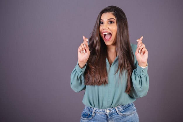 Foto horizontal Linda mulher brasileira com roupas casuais Jeans e camisa verde sinal de sorte dedos cruzados desejando