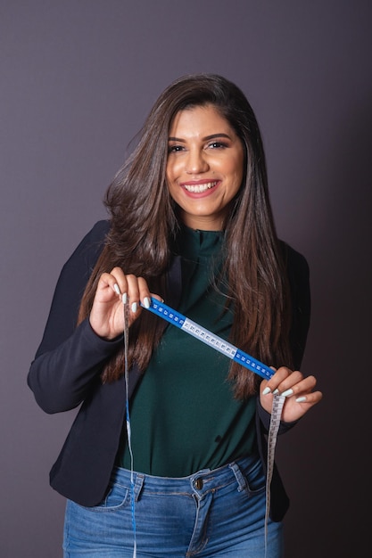 Foto horizontal linda mulher brasileira em roupas casuais blazer preto jeans segurando fita métrica nutricionista