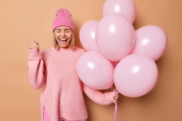 La foto horizontal de una mujer feliz se siente como si el ganador aprieta el puño y exclama en voz alta disfruta de la fiesta sostiene un montón de globos de helio celebra una ocasión especial en la vida. Sí, finalmente, graduación universitaria.