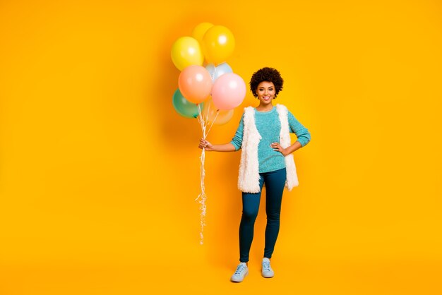 Foto in voller Größe von fröhlichen afroamerikanischen Mädchen halten Luftballons, die sie am Jubiläum bekommt tragen weiß blau flauschiges Outfit stilvolle trendige Schuhe über gelbe Farbe Wand isoliert