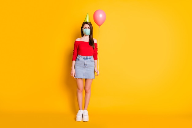 Foto in voller Größe von Mädchen in medizinischer Maske sozialer Distanz-Trend feiern Geburtstag allein halten Ballon tragen rote Jeansrockbeine Turnschuhe einzeln auf hell glänzendem Hintergrund