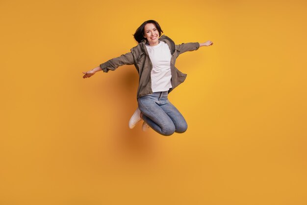 Foto in voller Länge der jungen Frau, die Fliegenhände hebt, die über gelbem Hintergrund isoliert springen