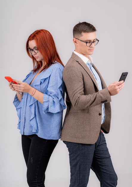 Foto in voller Länge eines jungen zufälligen Paares, das Rücken an Rücken steht und Telefonbildschirme betrachtet. Leute auf grauem Hintergrund.