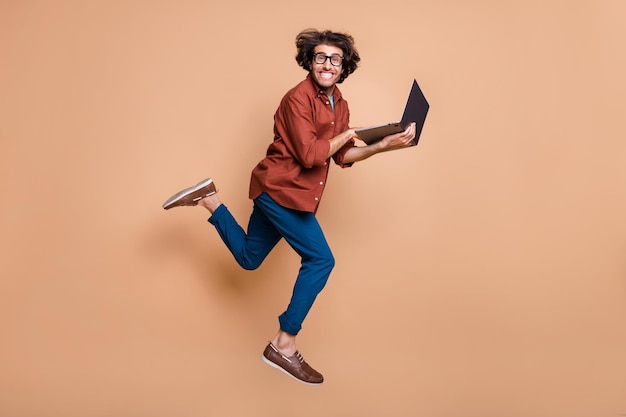 Foto in voller Länge Porträt eines Mannes, der einen Laptop hält und aufspringt, isoliert auf pastellbeigem Hintergrund