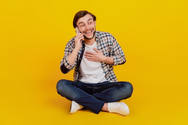 Foto in voller Länge von einem positiven fröhlichen Mann, der auf dem Boden sitzt