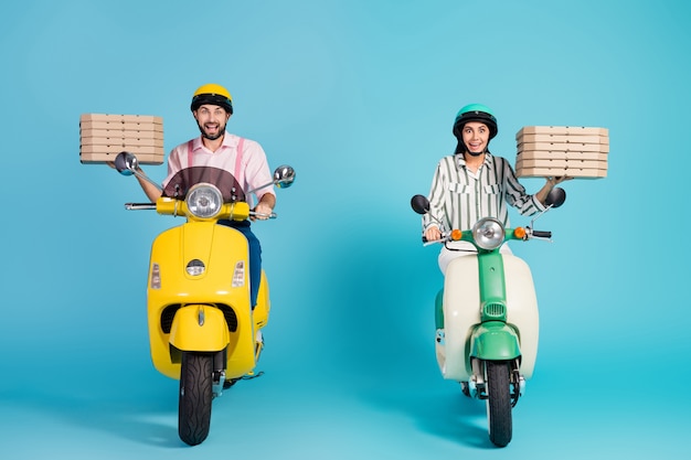 Foto in voller Länge von funky verrückten Dame Kerl fahren zwei Vintage Moped tragen Pizzaschachteln Kurier Beruf Junk Fastfood Formalwear Outfit Schutzhelm isoliert blaue Farbe Wand