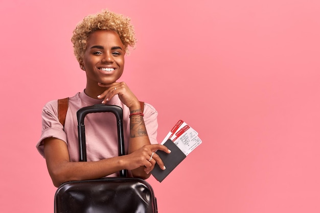 Foto interior de turista afro otimista com bagagem detém passaporte e bilhetes