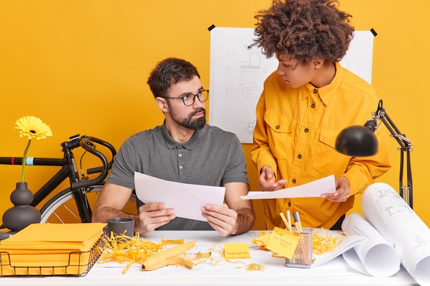 Foto interna de alunos habilidosos analisando erros de exame pose na mesa do escritório fazer lição de casa no espaço de coworking discutir algo. Dois colegas de trabalho, uma mulher e um homem, colaboram na confecção de rascunhos de projetos