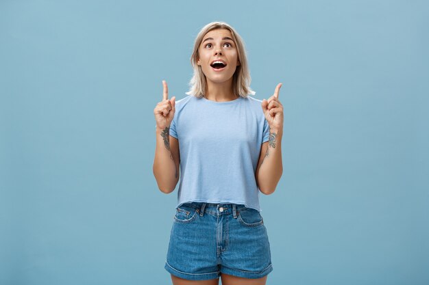 Foto interna de uma aluna loira atraente e sem palavras impressionada em uma camiseta casual e jeans