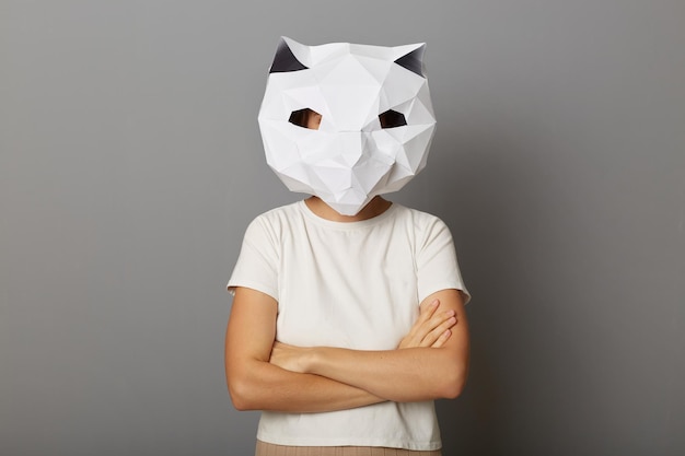 Foto interna de uma mulher orgulhosa e confiante usando máscara de papel de gato e camiseta branca posando isolada sobre fundo cinza em pé com as mãos postas expressando confiança